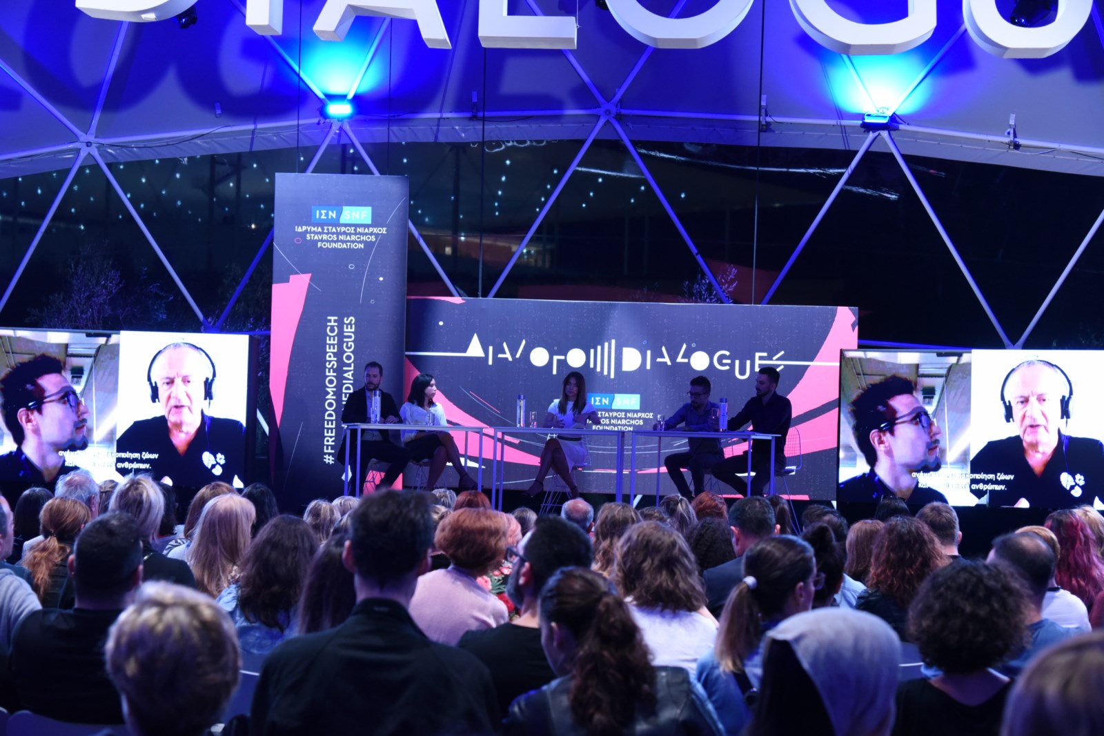 Ακροατές στη συζήτηση Διαλόγων ΙΣΝ που κοιτούν τη σκηνή όπου βρίσκονται πέντε ομιλητές.