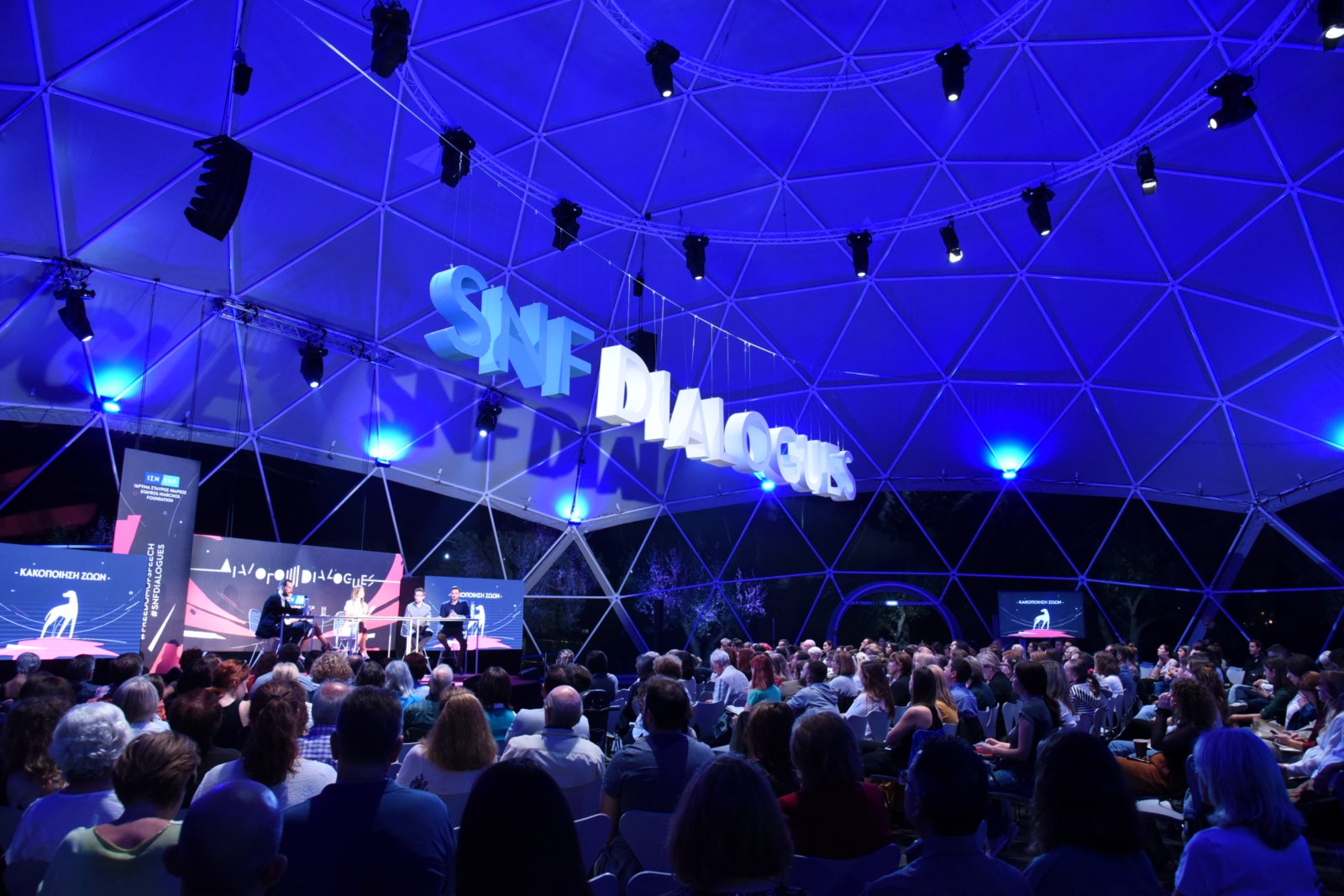 Ακροατές στη συζήτηση Διαλόγων ΙΣΝ που κοιτούν τη σκηνή όπου βρίσκονται πέντε ομιλητές.