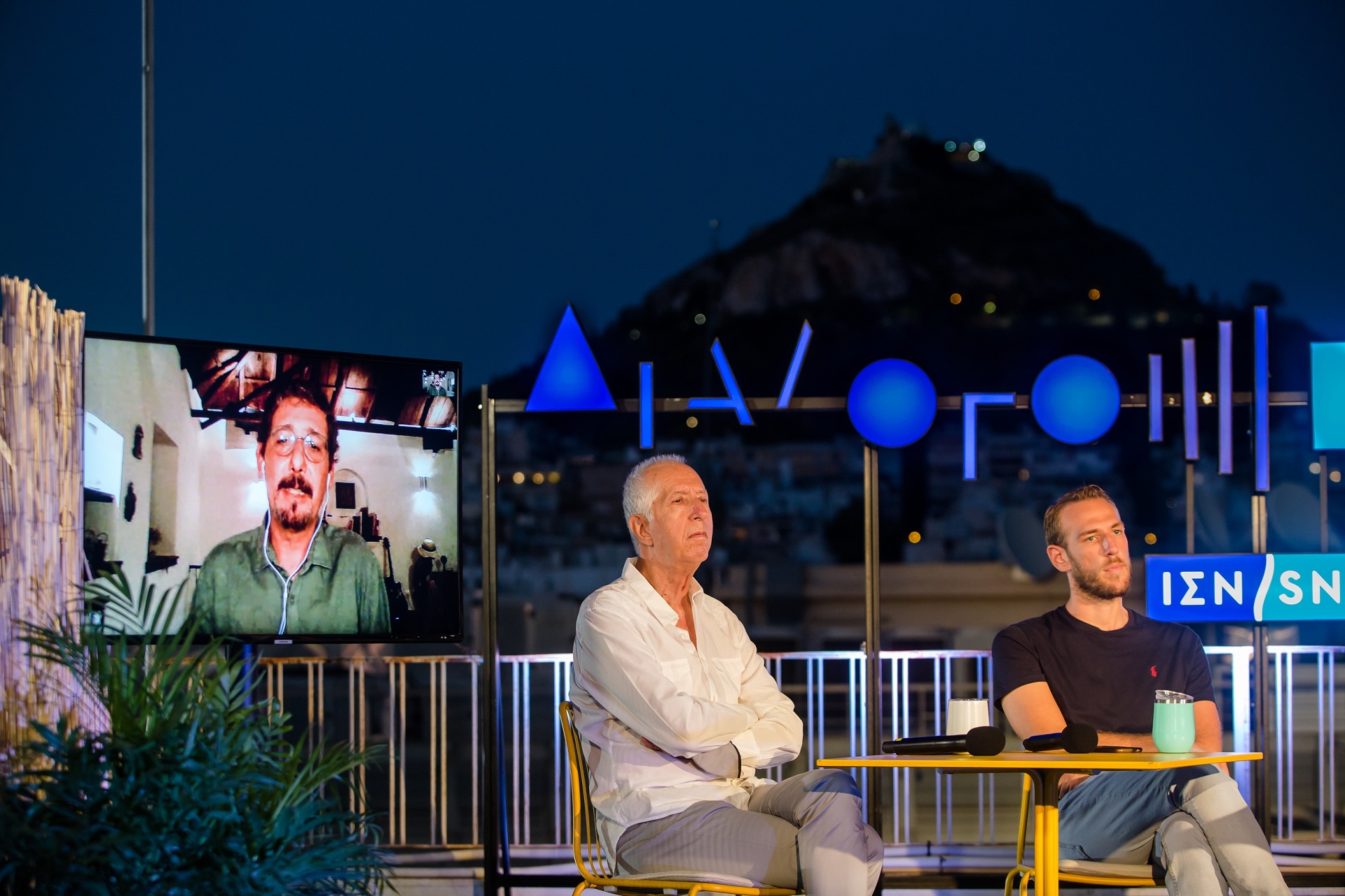 A screen showing a man and two guest speakers at the SNF Dialogues event.