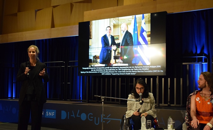 Τρεις ομιλητές στη σκηνή με μια μεγάλη οθόνη στη συζήτηση των Διαλόγων ΙΣΝ.