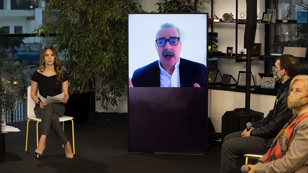 Anna Kynthia Bousdoukou next to a screen showing a man and the guest speakers at the SNF Dialogues event.