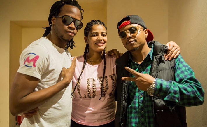 Two men wearing sunglasses and a woman in the middle posing for a photo