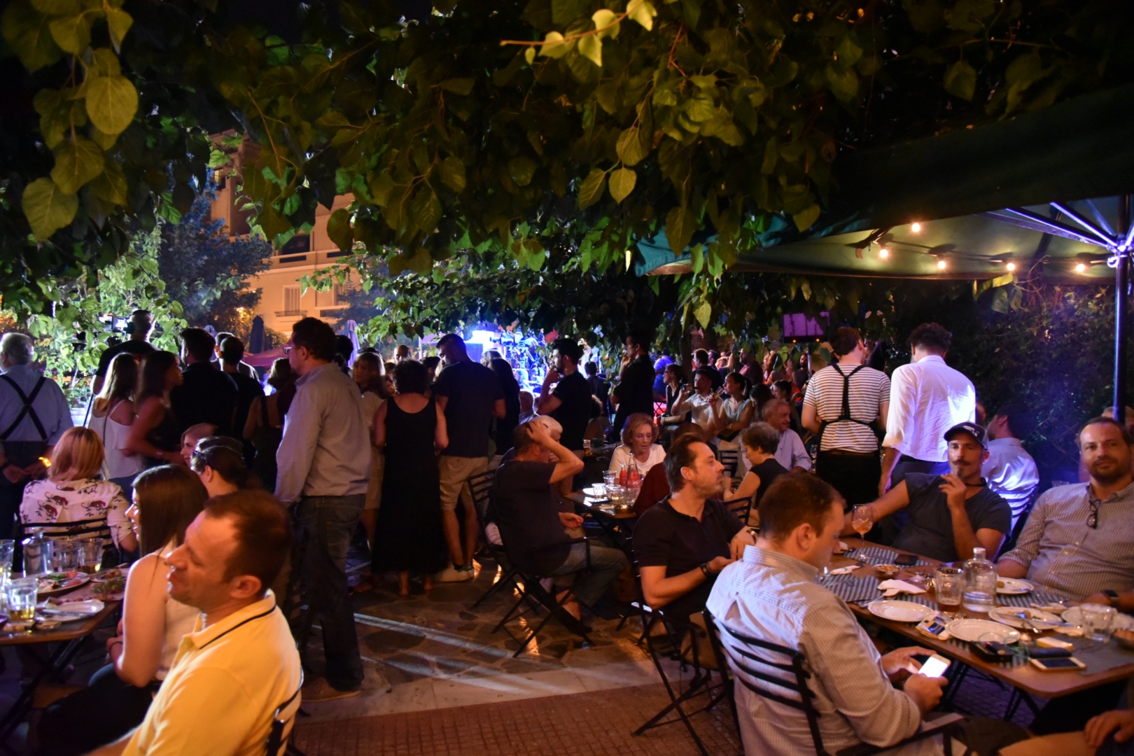 A diverse group of individuals sitting at tables in an outdoor area discussing and having fun.