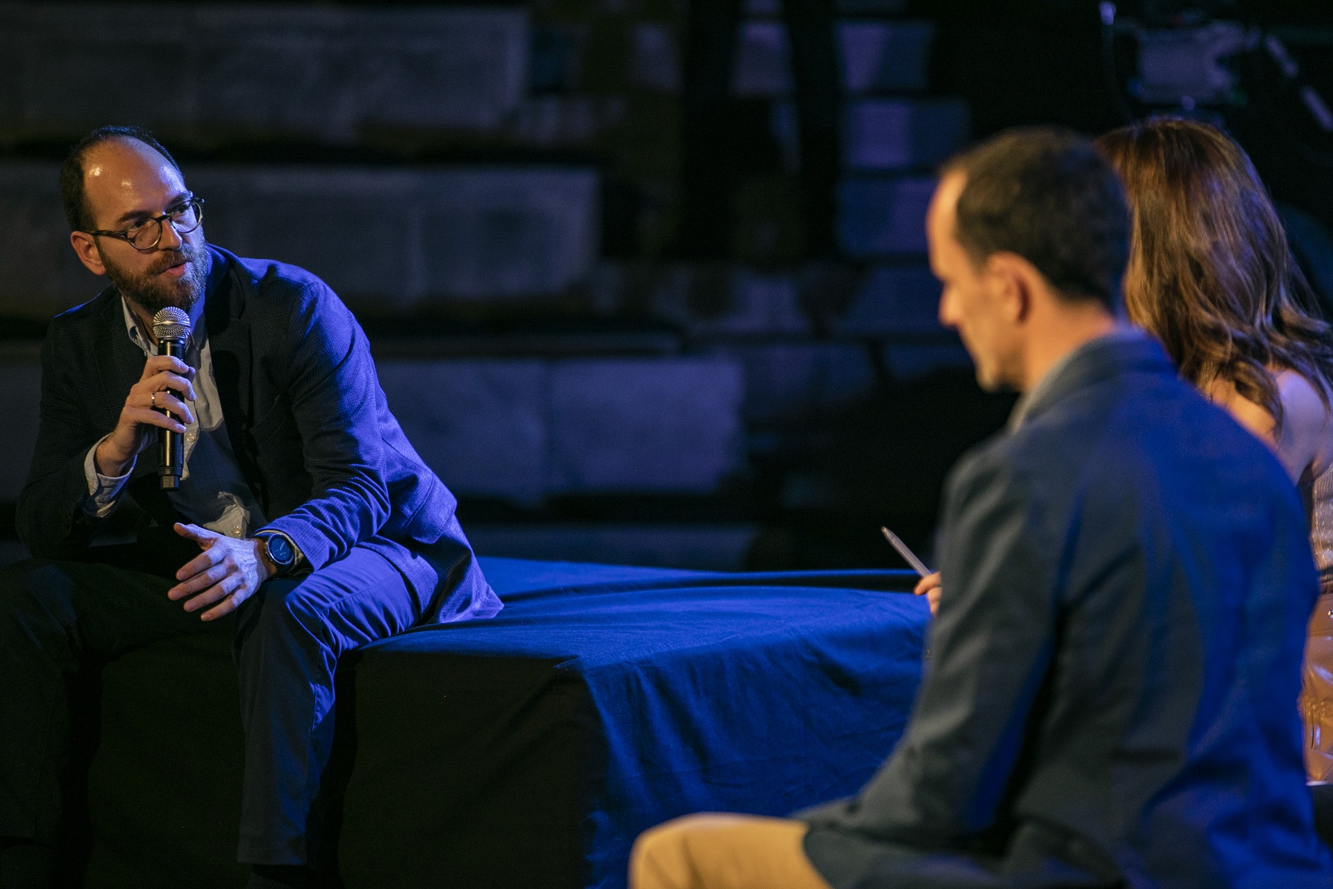 Speaker holding the mic and speaking to two other speakers at the SNF Dialogues event.