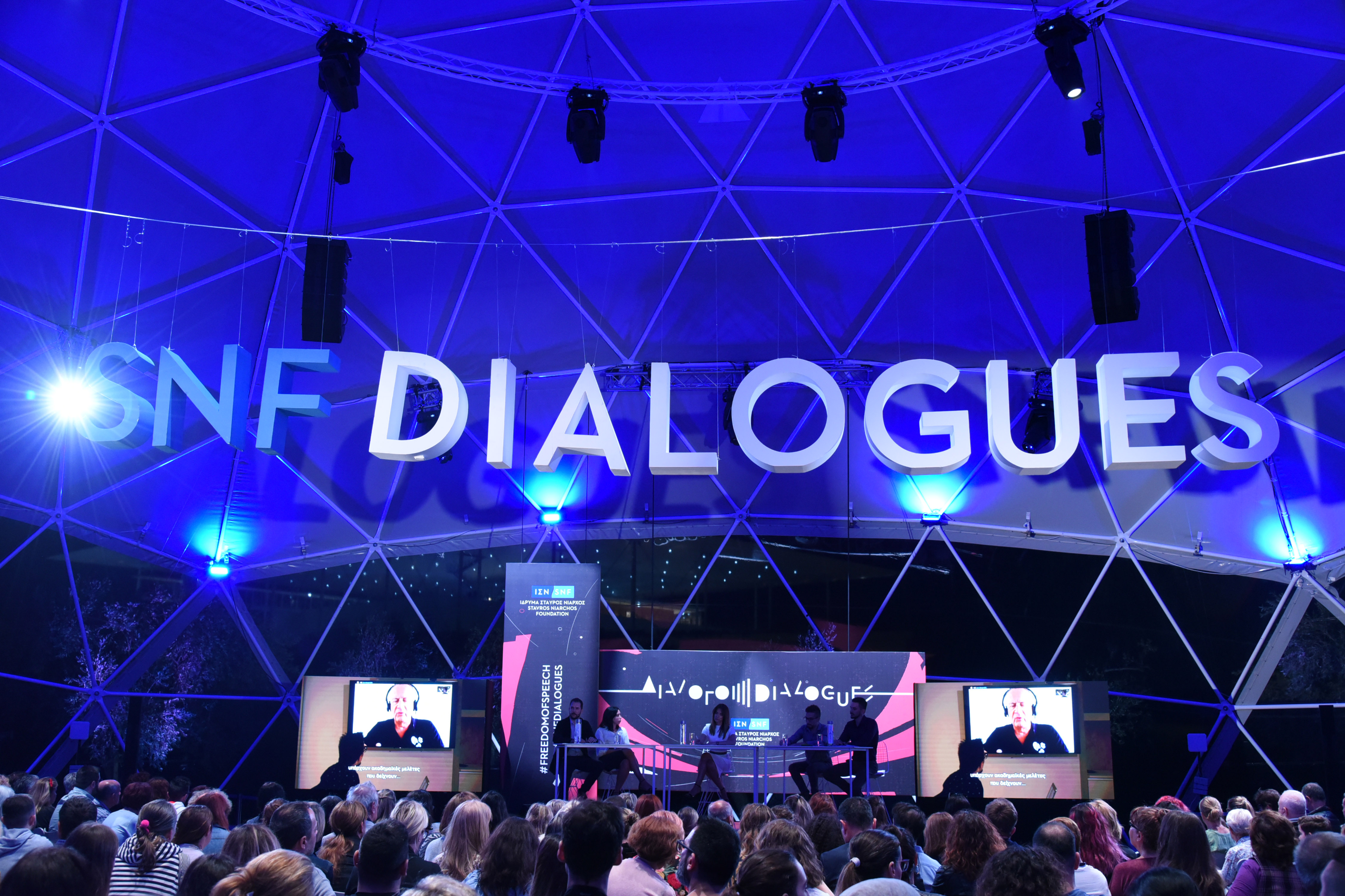 Ακροατές στη συζήτηση Διαλόγων ΙΣΝ που κοιτούν τη σκηνή όπου βρίσκονται πέντε ομιλητές.