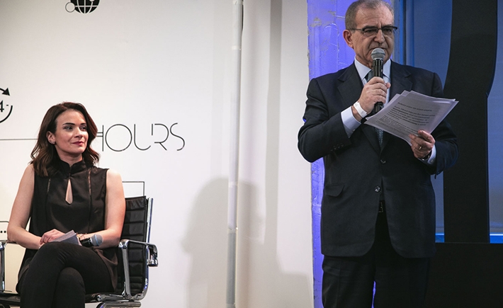 Ένας άνδρας όρθιος που μιλάει στο μικρόφωνο δίπλα στην Άννα-Κύνθια Μπουσδούκου στη συζήτηση των Διαλόγων ΙΣΝ