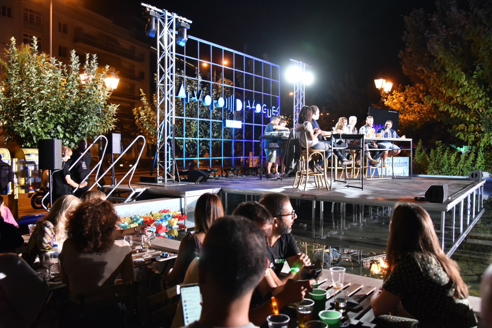 People seated at tables socializing while speakers are on stage at the SNF Dialogues event.