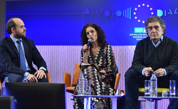Woman speaking on the microphone at the SNF Dialogues event with two other guests sitting beside her and listening