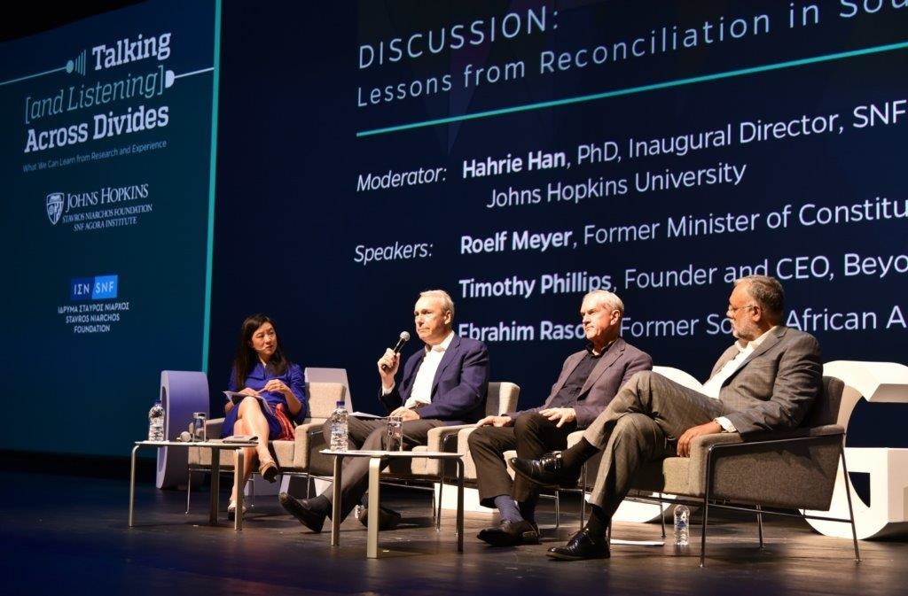 Τέσσερις καλεσμένοι ομιλητές στην σκηνή καθισμένοι μπροστά από ένα σκούρο φόντο στη συζήτηση των Διαλόγων ΙΣΝ