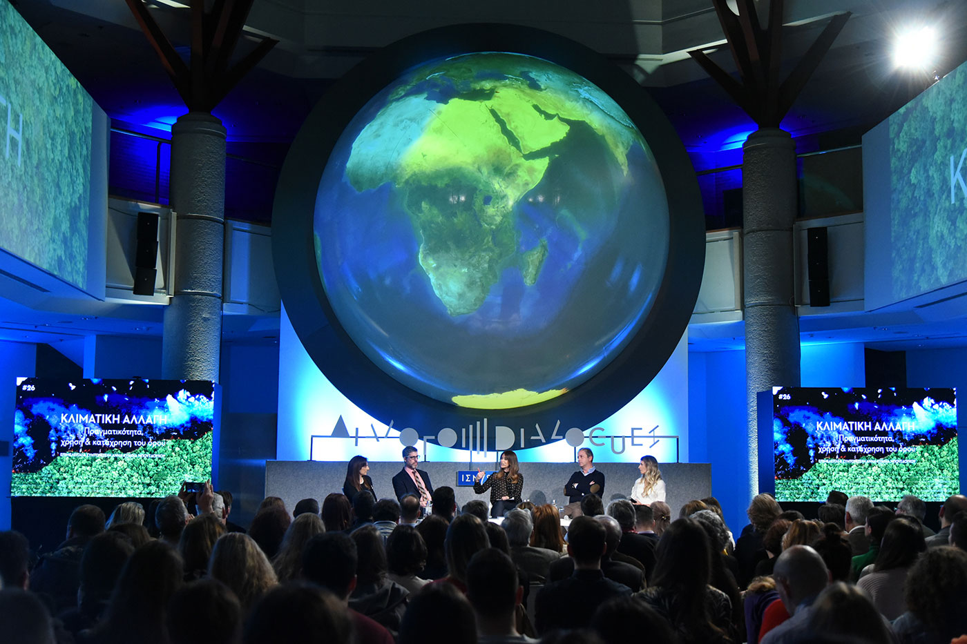 Anna-Kynthia Bousdoukou and the other guests on stage at the SNF Dialogues event and a large screen in the shape of the globe above