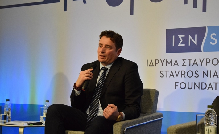 Άντρας ομιλητής καθισμένος σε πολυθρόνα κρατά ένα μικρόφωνο και μιλά στο κοινό στη συζήτηση των Διαλόγων ΙΣΝ.