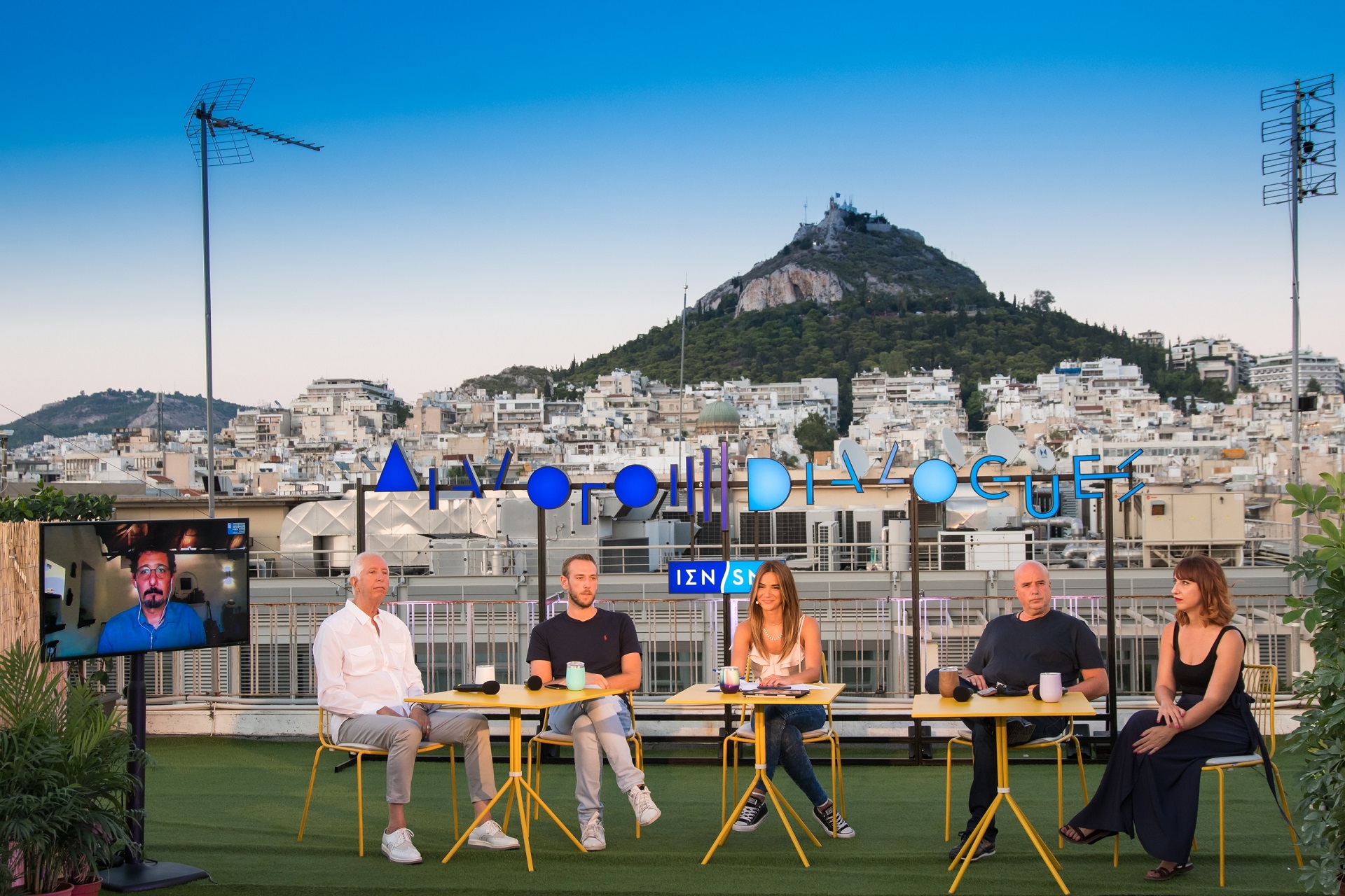 Anna Kynthia Bousdoukou , co-president A. Drakopoulos and three guest speakers with the Athenian landscape as a background at the SNF Dialogues event.