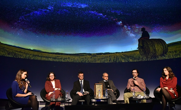 Έξι καλεσμένοι πάνω στην σκηνή στη συζήτηση των Διαλόγων ΙΣΝ με μια μεγάλη οθόνη πίσω τους
