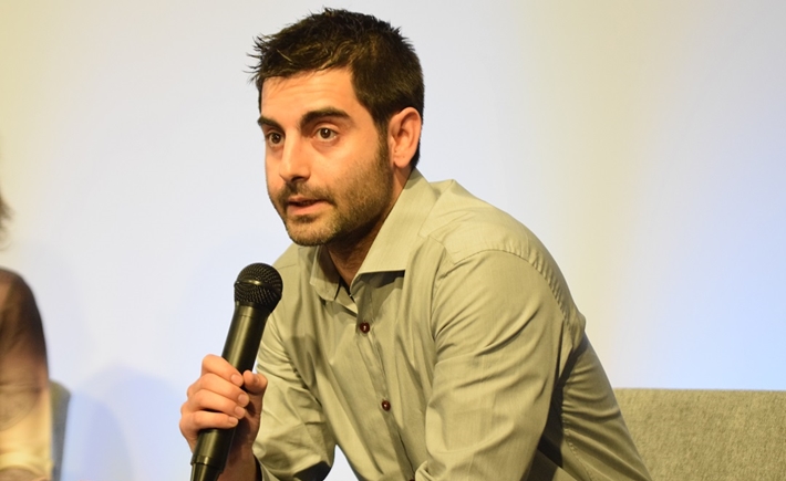 Άντρας ομιλητής καθισμένος σε πολυθρόνα κρατά ένα μικρόφωνο και μιλά στο κοινό στη συζήτηση των Διαλόγων ΙΣΝ.