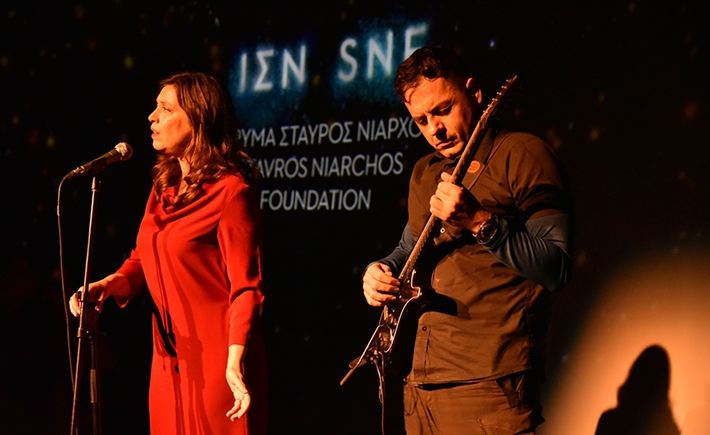 Μια γυναίκα που τραγουδάει και ένας άνδρας δίπλα της που παίζει κιθάρα πάνω στην σκηνή σε συζήτηση των Διαλόγων ΙΣΝ