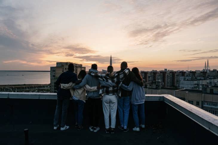 Group of six young people on rooftop, observing sunset.