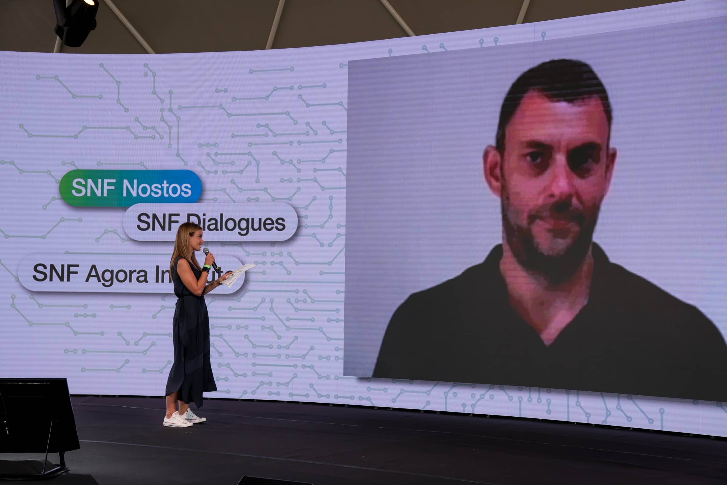 Anna Kynthia Bousdoukou on stage looking at the screen showing a man at the SNF Dialogues event.