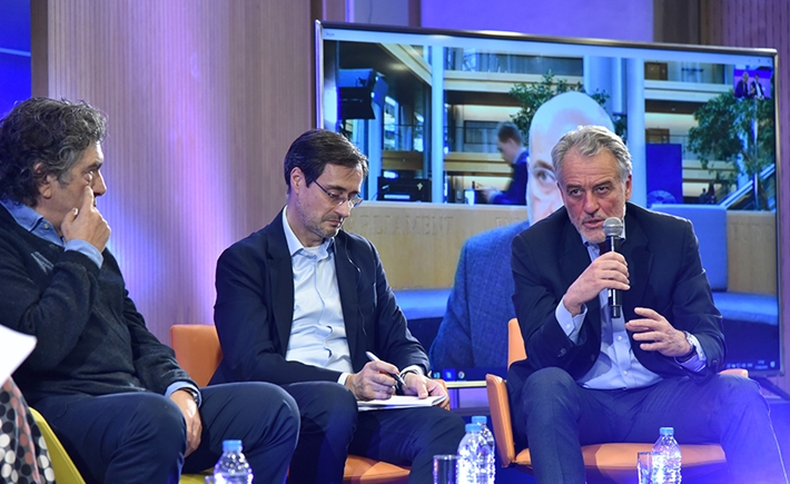 Three men speaking in front of a big screen speaking at the SNF Dialogues event