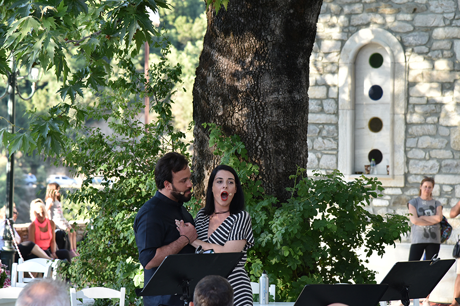 Ένας άνδρας και μια γυναίκα τραγουδούν μπροστά από ένα δέντρο στην πλατεία του χωριού μια ηλιόλουστη μέρα 